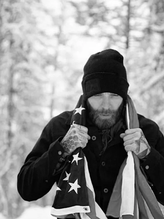 Man holding American flag in snowy forest.