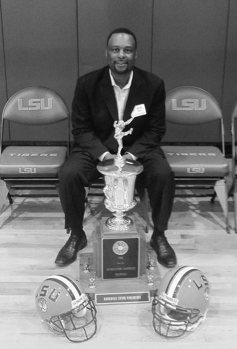 Man sitting with trophy and LSU helmets.